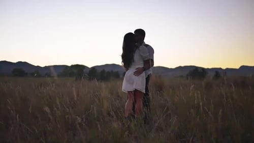 Biy and girl kiss in a field during sunset