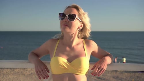 Attractive Woman in a Swimsuit and Sunglasses is Relaxing on the Sea Beach