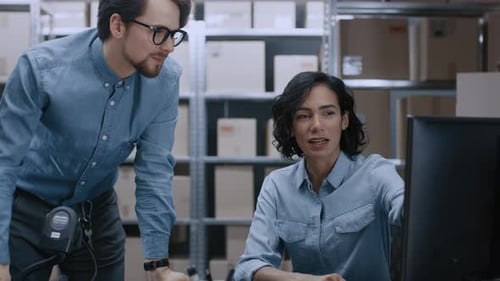 Male and Female Warehouse Inventory Managers Talking, Using Personal Computer and Checking Stock. I