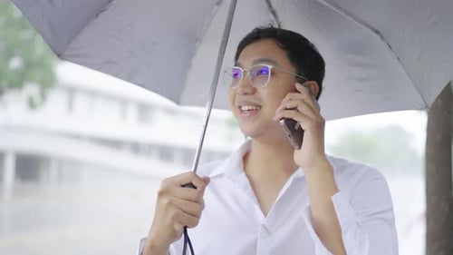 Happy carefree young man with umbrella standing in the city Rainy weather, talking on mobile phone,