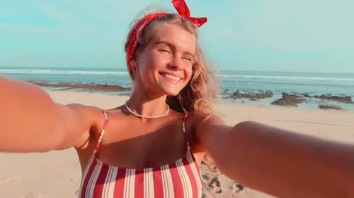 Young Caucasian Woman Holding Phone at Outstretched Hands Stands on Sunny Beach