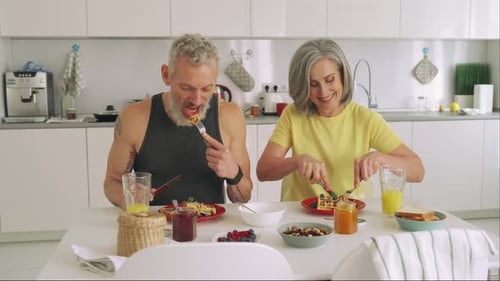 Pareja de familia mayor madura sana, feliz y en forma desayunando sentada en la cocina