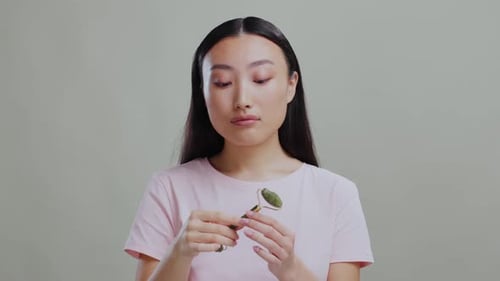 Young Pretty Asian Female Model Massaging Her Facial Skin with Green Jade Roller for Selfcare