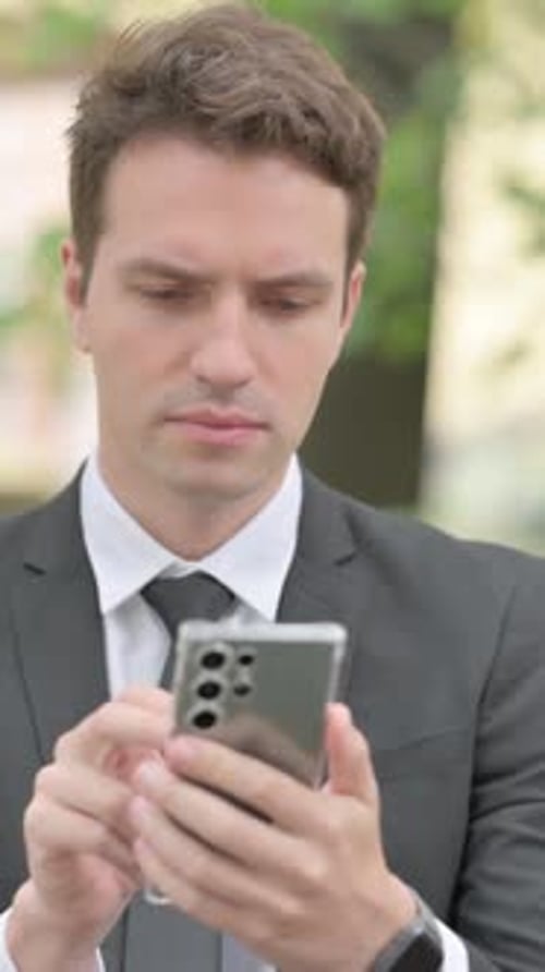 Man in Suit Typing on Phone in City Park