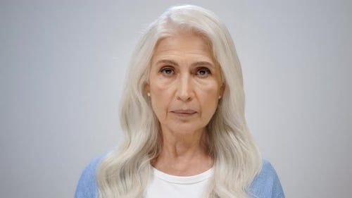 Elegant serious senior lady posing and raising head on a grey background in studio