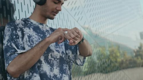 Young Man in Headphones Using Smartwatch and Running in City