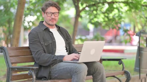 Smiling Man Working on Laptop in Sunny Park