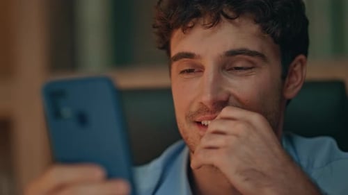 Carefree Freelancer Browsing Video Content at Cellphone in Evening Home Close Up