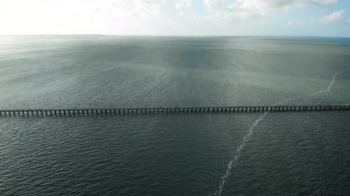 Push and fast camera tilt towards long, wooden pier stretching outwards into the great expanse of da