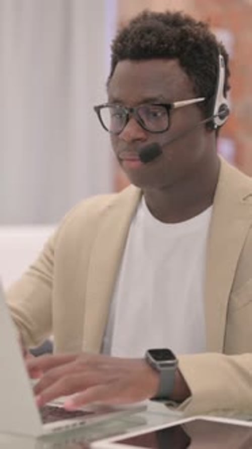 Professional Man Typing on Laptop Wearing Headset Indoors
