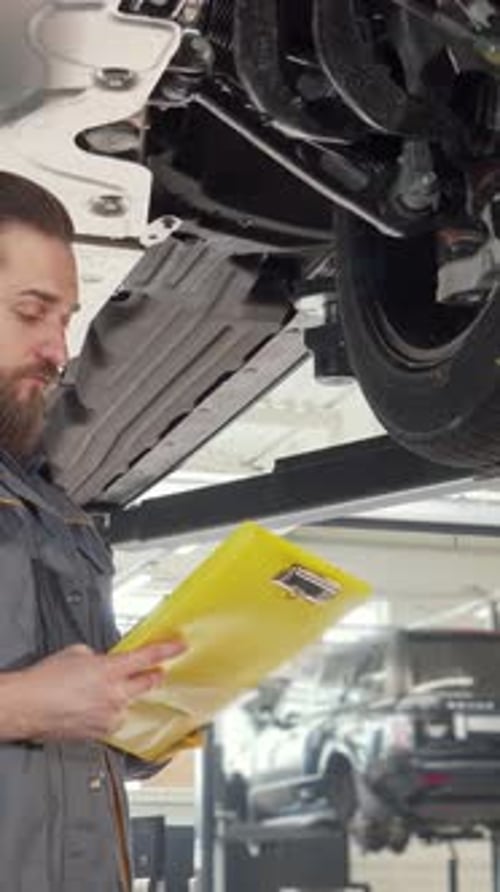 Focused Mechanic Inspecting Lifted Vehicle While Taking Notes