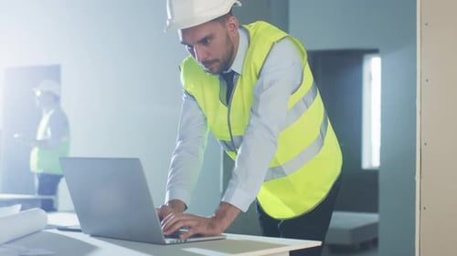 Ingenieur mit Schutzhelmen benutzt Laptop in einem im Bau befindlichen Gebäude.
