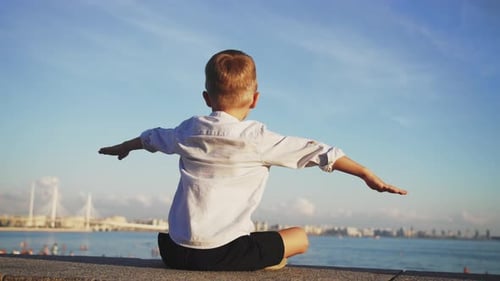 Enfant garçon assis sur un remblai au bord de l'eau dans le centre de la ville de St.