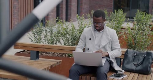 Businessman Sitting Outdoors and Working with Laptop Typing Concentrated on Professional Activity