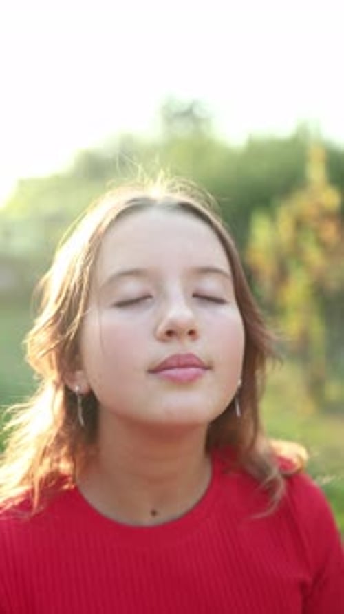 Une fille profite de la chaleur du soleil debout dans un jardin entouré de plantes vertes et d'une clairière