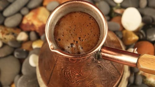 Traditional rich Turkish coffee boiling in a copper Jezve pot on pebbles