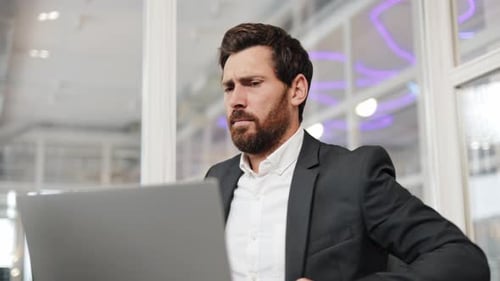Businessman Stretches At His Desk While Working On Laptop In Office