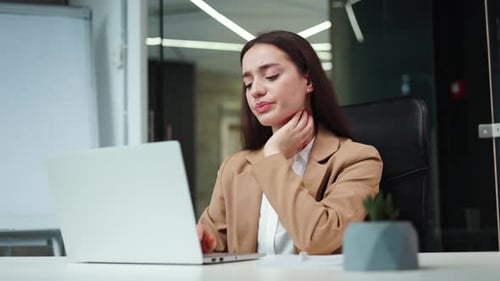 Frustrated Woman Feeling Pain in Neck While Sitting at Office Desk with Laptop