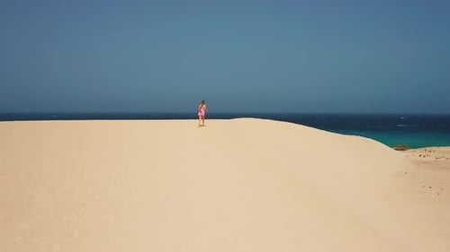 Woman Walks Alone on Sand Dune by Ocean