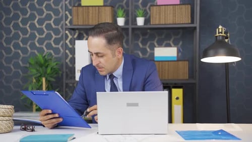 Businessman at Desk Working with Laptop and Paperwork