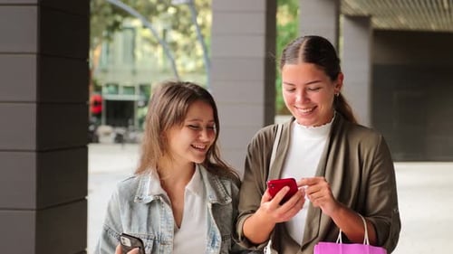Young Women Look at Smartphone Together in City