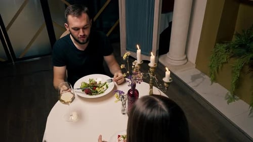 Portrait of a young guy with a beard eating salad in an Italian restaurant during a date with girl