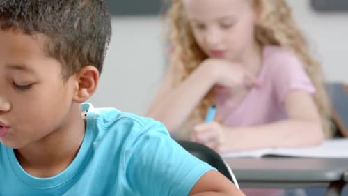 Caucasian girl with curly blonde hair is focused on writing in a classroom at school