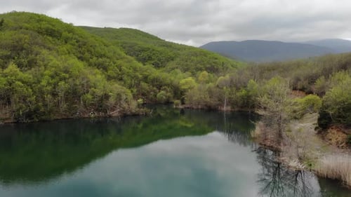 Drone video low flight over lake at mountain forest sunny overcast