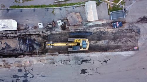 Construction work on city road from aerial top down shot. Excavator digging trench into asphalt. Hea
