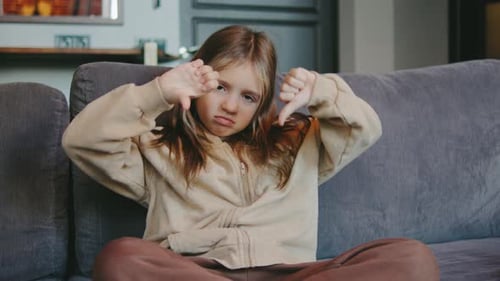Sad Girl Gives Thumbs Down on Sofa at Home