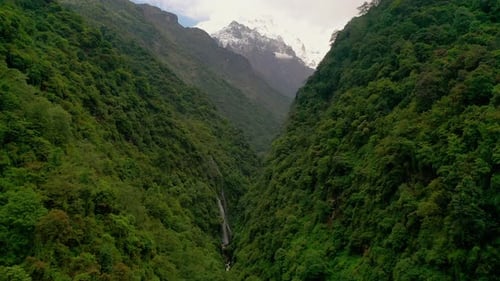 Scenic aerial drone view flying through a lush mountain valley in the Himalayas.