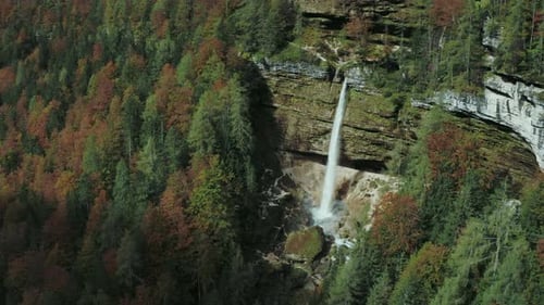 Aerial view of a big waterfall in mountains surrounded by forest in fall autumn.