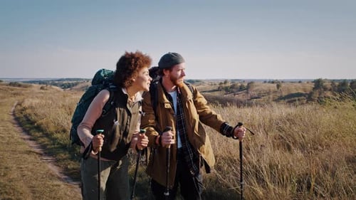 Young Mixed Race Couple with Walking Poles Hikes in Field