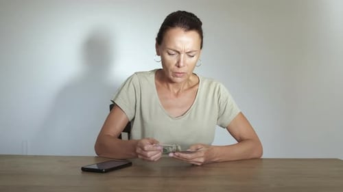 Worried Woman Counts Money at a Table