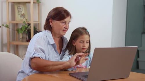 Grandmother and Granddaughter Video Chatting on Laptop Indoors