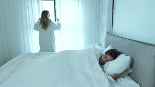 Woman Opens Curtains as Man Sleeps in Bed