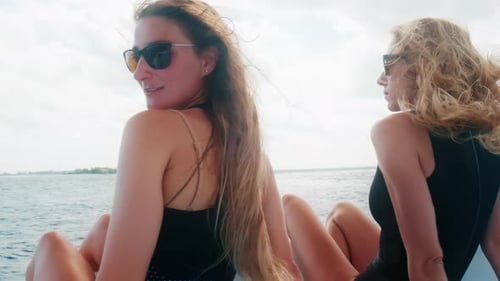 Frauen auf dem Boot. Zwei junge Frauen in schwarzen Anzügen entspannen sich auf dem Dach des Bootes, das sich im Meer bewegt