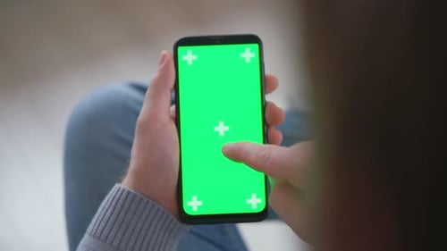 Young Man Sitting at Home Holding Smartphone Green Mockup Screen in Hand Male Person Using Chroma