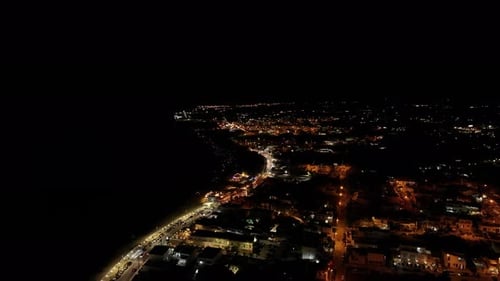 Stunning 4K drone footage of the sea at night, with illuminated coastline and city lights