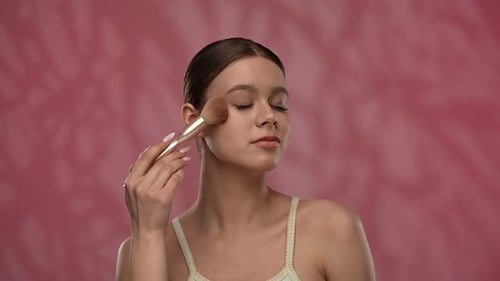 Young Woman with Makeup Posing at Camera in Studio Playfully Smiling Touching Applying Blushes with