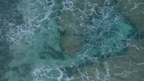 Top Down Slow Motion Drone View of turquoise clear water and crashing waves over shallow coral reef