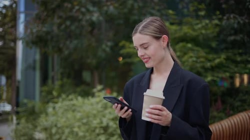 Woman Using Phone with Coffee in City Park