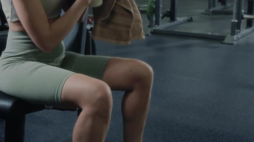 Woman Resting on Gym Bench and Drinking Water after Training