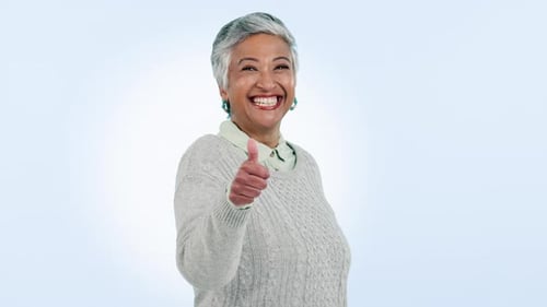 Face, gesture and senior woman with thumbs up, agreement and feedback on blue studio background