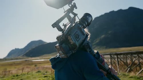 Filmmaker Carrying Camera and Tripod in Rural Landscape