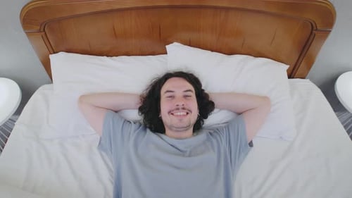 A Young Man with Curly Hair Falls Into Bed with Excitement Viewed From Above His Carefree Motion and