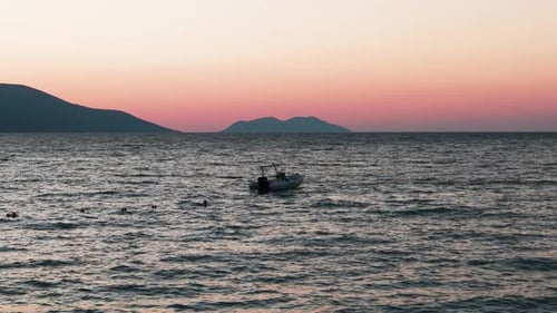 Calm view of floating boat on sea with sunset color mountain silhouette