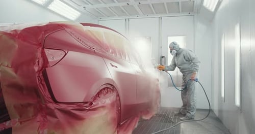 Car Painter Spraying Clear Coat in Bright Auto Shop