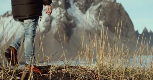 Man Explores Black Sand Beach With Snowy Mountains Behind