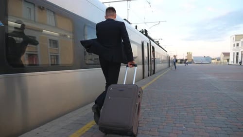 Man in Suit Pulling Suitcase Alongside Modern Train